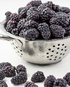 a colander full of blackberries on a white table