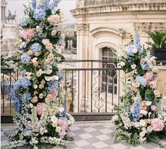 two tall floral arrangements sitting on top of a tiled floor in front of a building