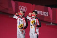 two olympic athletes standing next to each other with their hands on their faces and medals in front of them