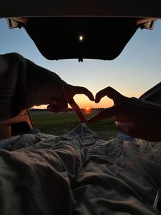 someone making a heart with their hands in the back of a car at sunset or dawn