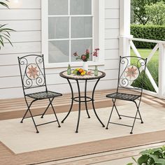 two chairs and a table on a porch with flowers in vases next to it