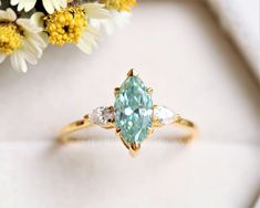 an aqua and white diamond ring sitting on top of a table next to some flowers