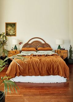 a large bed sitting on top of a hard wood floor next to a plant in a bedroom