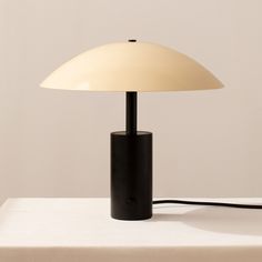 a black table lamp with a white shade on it's head and cord attached to the base