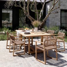 a wooden table with chairs around it on a brick patio next to a large tree