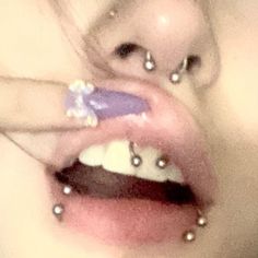 a close up of a person with piercings on her nose and hand holding an object in their mouth