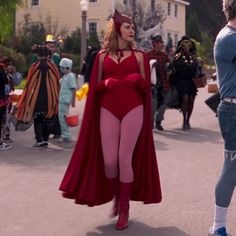 a woman in a red costume is walking down the street with other people behind her