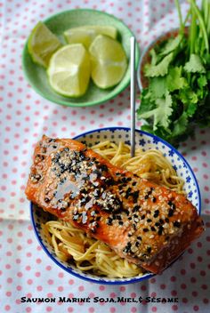 salmon and noodles in a bowl on a table with lemons, cilantro and parsley