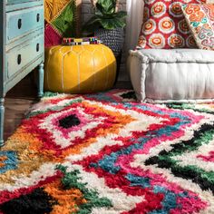 a colorful rug in the corner of a room next to a dresser and potted plant