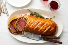 a plate with meat and bread on it next to two glasses of wine, spoons and utensils