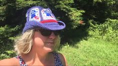 a woman wearing a blue hat and sunglasses in front of some grass with trees behind her