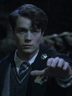 the young man is pointing at something with his finger in front of him and wearing a harry potter jacket