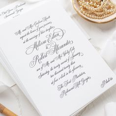 the wedding stationery is laid out on top of white paper with pearls and beads