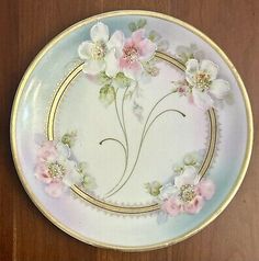 a white plate with pink flowers and gold trimmings on the edge, sitting on a wooden table