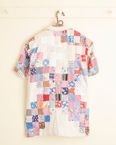 an old patchwork shirt hanging on a hook in front of a white wall with a wooden hanger