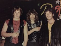 three young men standing next to each other in front of a wall with graffiti on it