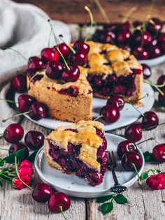 two plates with cherry pie on them and cherries around the edges, along with one slice missing