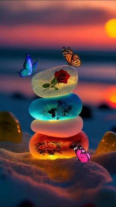 a stack of rocks sitting on top of a beach covered in sand with butterflies flying over it