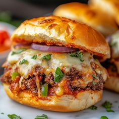 two hamburgers with meat and cheese on them sitting on a plate next to some bread buns