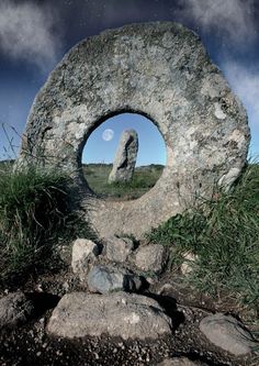 a rock with a hole in the middle surrounded by grass and rocks