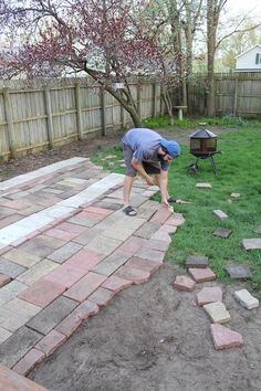 a man bending over to pick up something from the ground in his backyard garden area