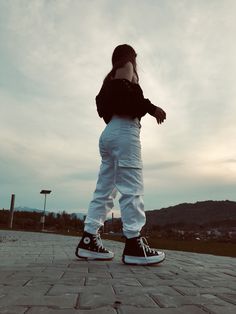 a girl in black shirt and white pants standing on brick ground with her hands behind her head