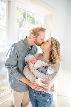 a man and woman kissing while holding their baby in front of a window with the light coming through them