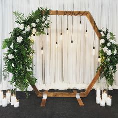 a wedding arch decorated with greenery, candles and white flowers on the floor in front of a curtain