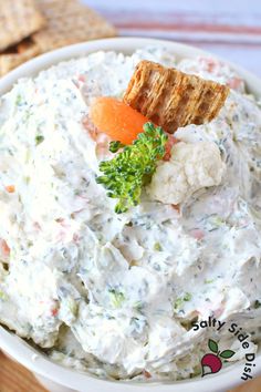 a white bowl filled with carrots, broccoli and cauliflower next to crackers