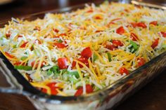 a casserole dish with cheese, tomatoes and lettuce in it on a wooden table