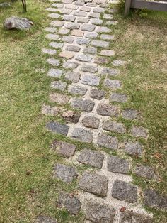 a stone path in the middle of a grassy area next to a bench and tree