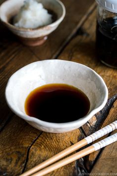 two chopsticks are next to a bowl of food on a wooden table with rice and sauce in it