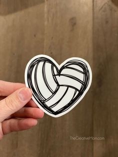 a hand holding up a sticker with a heart shaped volleyball ball in the middle