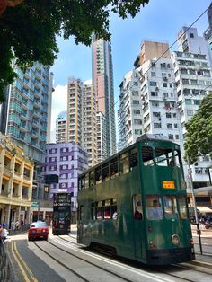 a green double decker bus driving down a street next to tall buildings in the city