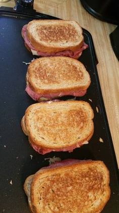 three toasted sandwiches sitting on top of a black pan covered in cheese and meat