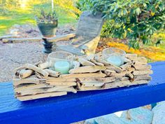 two candles are sitting on driftwood in front of a potted plant and bench