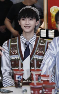 a young man wearing a tie and vest in front of other people at a table