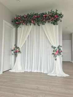 a white backdrop with pink flowers and greenery on it is in the middle of a room