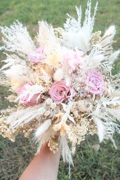 a bridal bouquet in someone's hand with pink roses and feathers on it