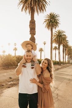 a man and woman holding a baby in front of palm trees