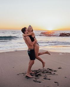 a man and woman hug on the beach as the sun sets