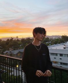 a young man standing on top of a balcony next to a building with the sun setting in the background