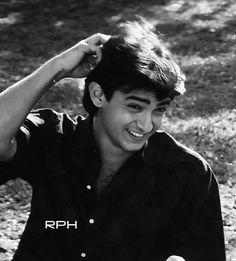 a young man sitting on the ground holding his hair in one hand and smiling at the camera