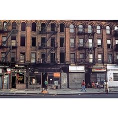 people walking down the street in front of an old building with fire escapes on it