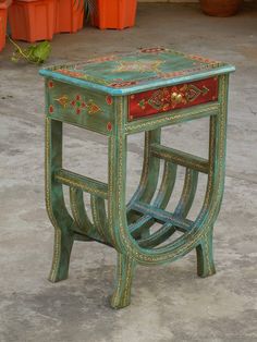 a green table with red and gold designs on the top sitting in front of potted plants