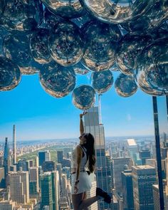 a woman standing on top of a tall building with lots of shiny balls hanging from the ceiling