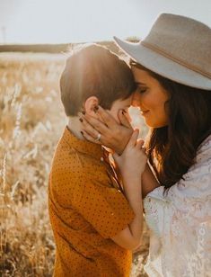 a woman hugging a boy in a field with the sun shining on her and he is wearing a hat