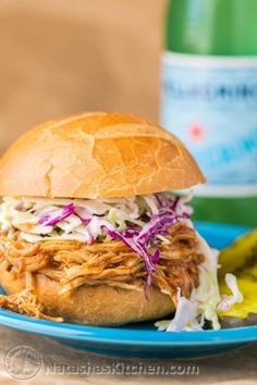 a pulled pork sandwich with coleslaw and pickles on a blue plate next to a bottle of water