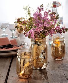 three mason jars filled with flowers on top of a wooden table next to plates and utensils