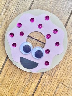 a pink doughnut with googly eyes and purple sprinkles on it